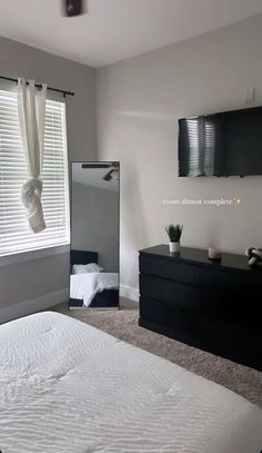 a bedroom with a bed, dresser and mirror in the corner next to a window