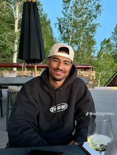 a man sitting at an outdoor table with a glass of wine in front of him