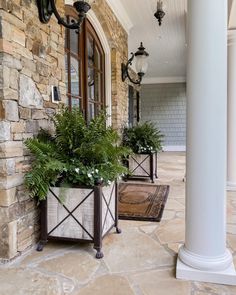 two planters on the front porch of a house with stone pillars and doors in the background