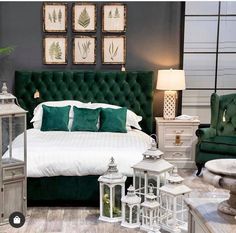 a bedroom with green velvet headboard, white bedding and lots of lanterns on the floor