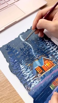 someone is painting a house on paper with a brush and watercolor pencils in front of a laptop computer