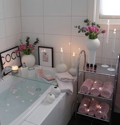 a bath tub with candles and flowers in the corner, next to a vase filled with pink roses