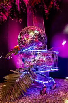 a disco ball sitting on top of a shopping cart in front of a tree with purple lights