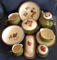 a collection of green and white dishes with strawberries painted on the plates, cups and saucers