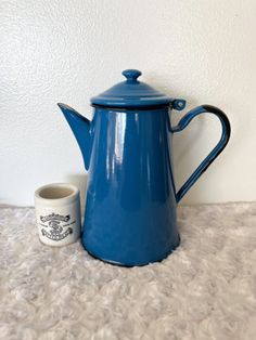 a blue tea pot next to a mug on a white carpeted floor in front of a wall