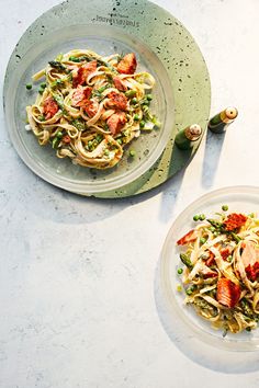 two plates filled with pasta and vegetables on top of a white tablecloth next to each other