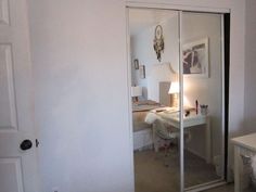 a bedroom with a desk and mirror in the corner, next to a closet door