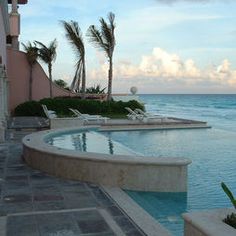 an outdoor swimming pool next to the ocean with palm trees in the foreground and blue sky