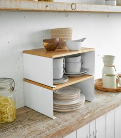 plates and bowls are stacked on top of each other in a kitchen shelf with wooden shelves