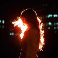 a woman standing in the dark with her hair blowing back and bright light shining on her face