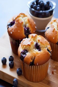 three blueberry muffins on a wooden cutting board