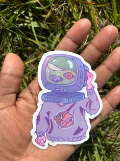 a hand holding a purple sticker with an image of a spaceman on it