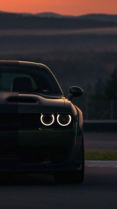 the front end of a black sports car with its lights on at sunset or dawn