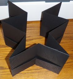 three pieces of black paper sitting on top of a wooden table