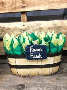 a basket filled with green flowers sitting on top of a wooden table next to a sign