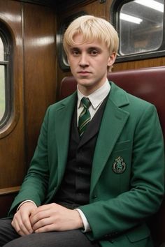 a young man in a green suit and tie sitting on a train seat looking at the camera