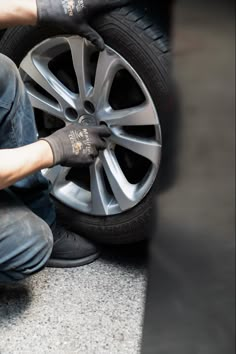 a man working on the tire of a car with rubber gloves and wrench next to it