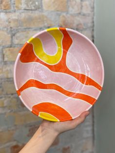 a hand holding a pink and yellow bowl with an orange swirl design on the bottom