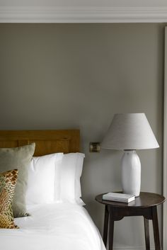 a bed with white sheets and pillows next to a table with a lamp on it