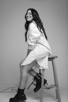 a black and white photo of a woman sitting on a stool with her legs crossed