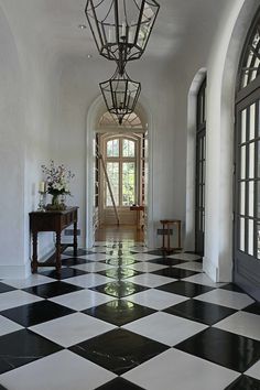 a hallway with black and white checkered flooring, chandelier and windows