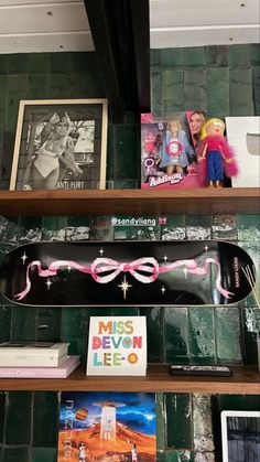 a shelf filled with books and toys on top of a green tiled wall next to pictures