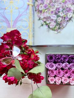 a vase filled with pink and red flowers next to a box of purple paper roses