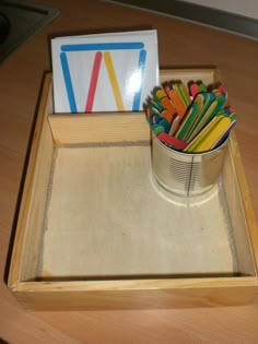 a cup filled with colorful pencils sitting on top of a wooden table next to a sign