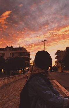 a person sitting on a bench looking at the sky with buildings in the background as the sun sets