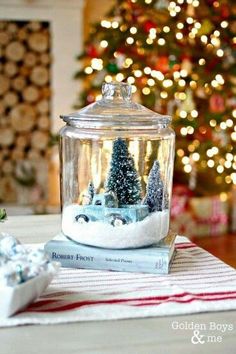 a glass jar filled with snow sitting on top of a table next to a christmas tree