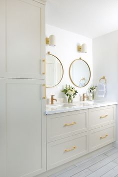 a white bathroom with two sinks and gold accents on the mirrors above them is shown