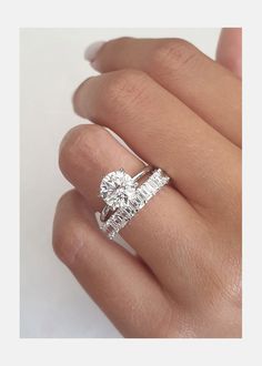 a woman's hand with a diamond ring on top of her finger and the other hand holding an engagement ring