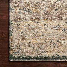 a beige and green rug on top of a wooden floor with dark wood floors in the background