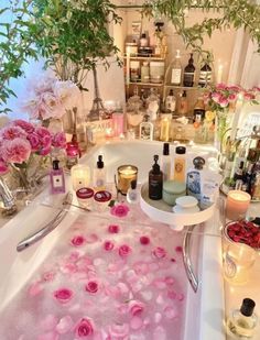 a bathtub filled with lots of flowers and candles next to a sink full of bottles