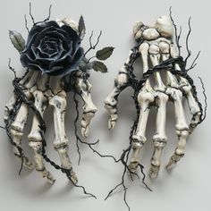 two fake skeleton hands holding a black rose with leaves on it's sides, one is broken and the other has fallen apart