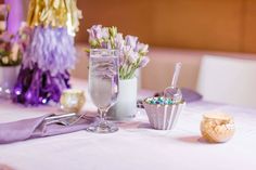 the table is set with purple and white flowers in vases, silverware, candy bars, and champagne flutes