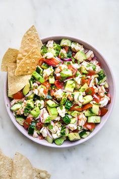 a bowl filled with cucumber, tomatoes and other vegetables next to tortilla chips