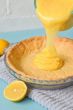 a person pouring sauce into a pie crust in a glass bowl with lemons around it