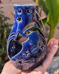 a hand holding a small blue vase in it's palm