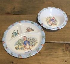 two plates with peter rabbit designs on them sitting on a wooden table next to each other