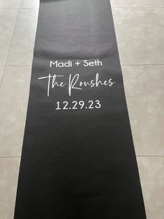 a black mat with the names and date printed on it is sitting on a tile floor