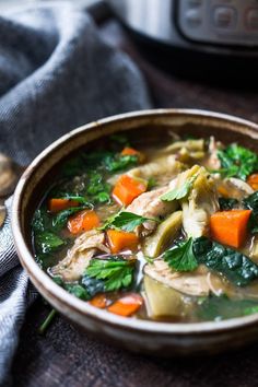 a bowl of soup with carrots, spinach and meat in it on a table next to an instant pressure cooker