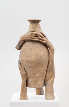 a large clay vase sitting on top of a white pedestal with hands covering it's face