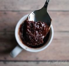 a spoon filled with chocolate pudding on top of a white cup next to a wooden table