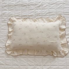 a white pillow with ruffled edges on top of a quilted bedspread