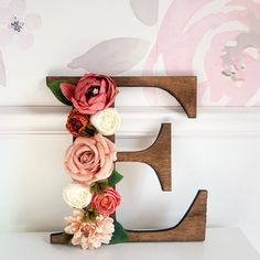 a wooden letter decorated with flowers on top of a white shelf next to a wall