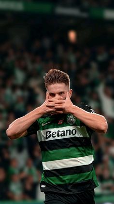 a soccer player covers his face with his hands as he stands in front of an audience