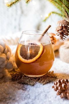 a glass filled with liquid sitting on top of a table next to pine cones and christmas decorations