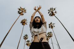 a woman reaching up into the air with her hands in the air and palm trees behind her