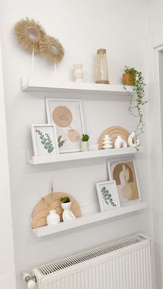 two white shelves with pictures and plants on them in a room next to a radiator